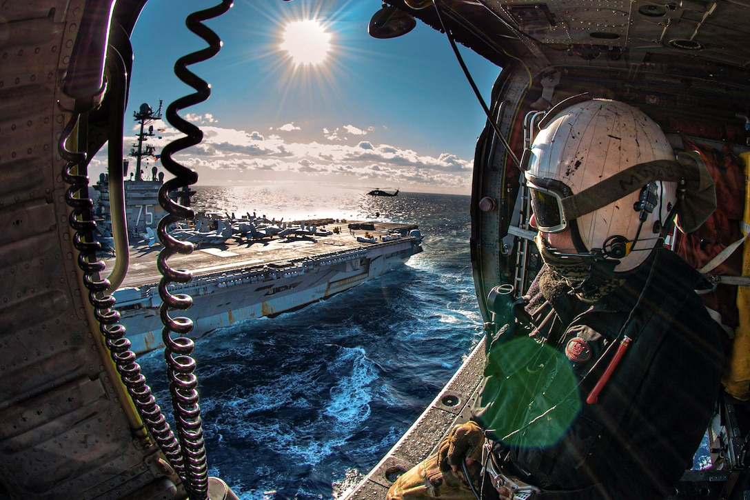 A sailor sitting in a helicopter looks at ship at sea.