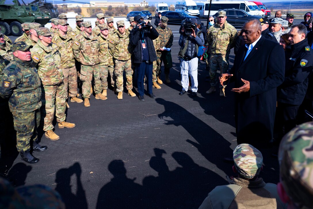 Defense Secretary Lloyd J. Austin III speaks to U.S. and NATO troops in a semi-circle.