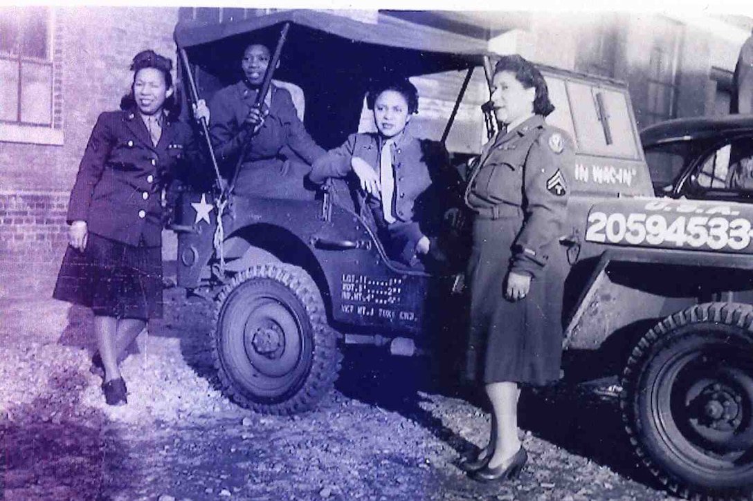 Two women sit in a Jeep while two other women stand beside it.