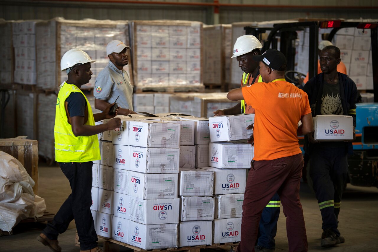 Workers move USAID boxes in a warehouse