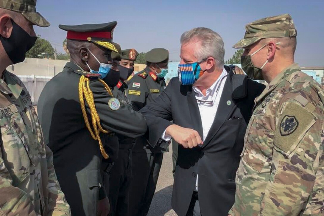 A U.S. civilian bumps elbows with a foreign officer outside.