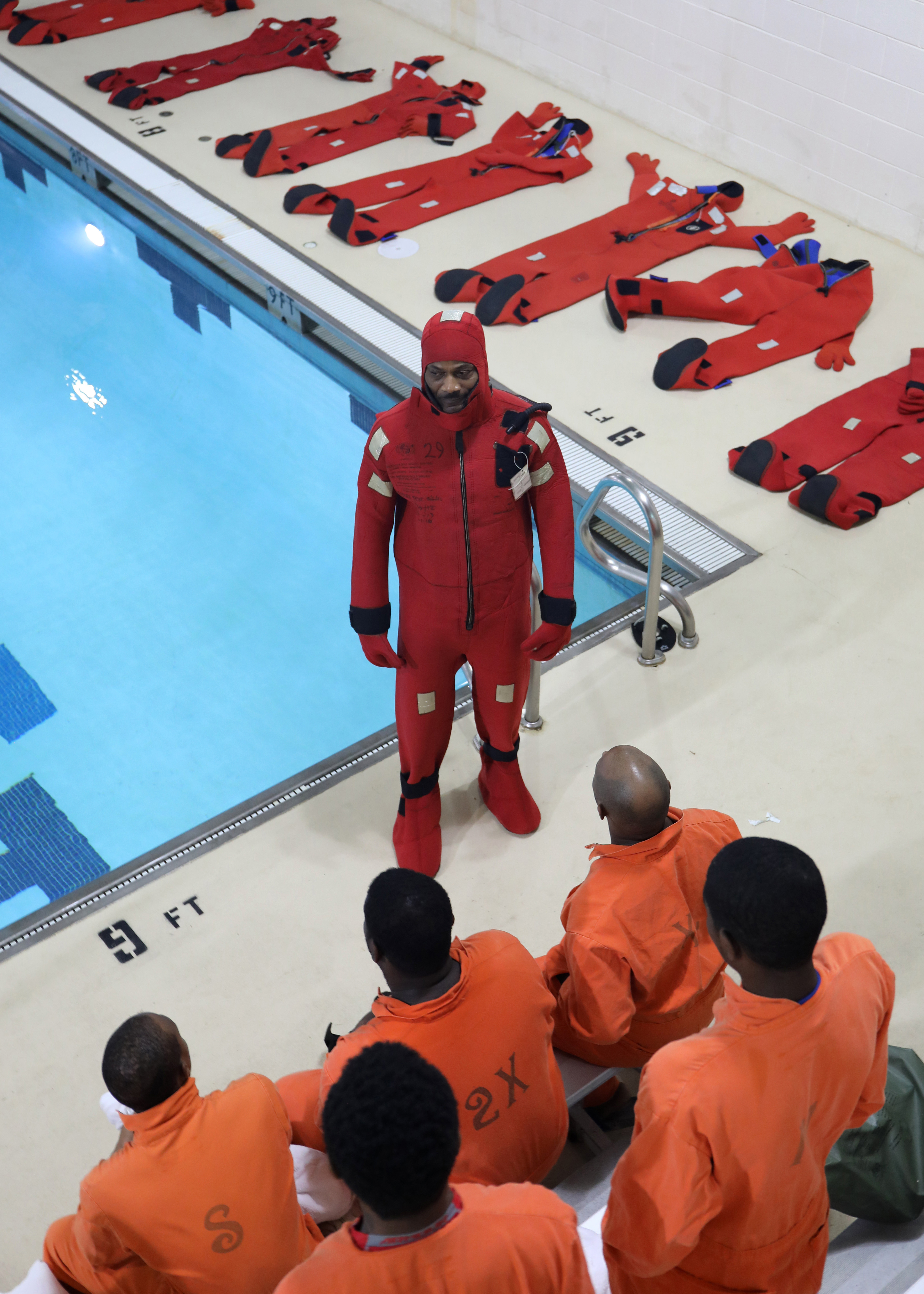 Andre Sutten, an instructor at Military Sealift Command Training Center East, demonstrates the proper donning of an at-sea survival suit to newly hired Civil Service Mariners (CIVMAR) during an abandon ship scenario at the training center on Joint Base Langley-Fort Eustis, Virginia, Feb. 25.