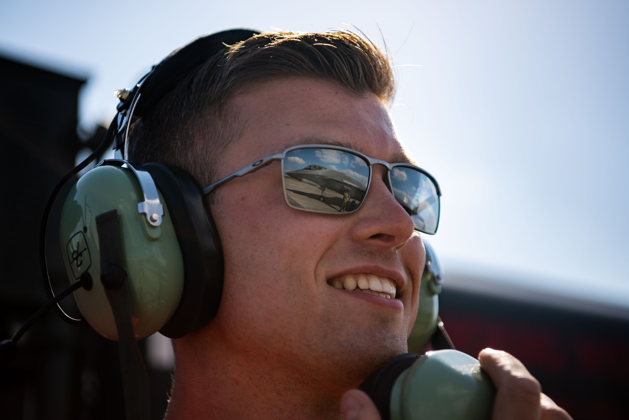 An Airman smiles with a reflection of hot pit refueling a F-35A Lightning II in his sunglasses.