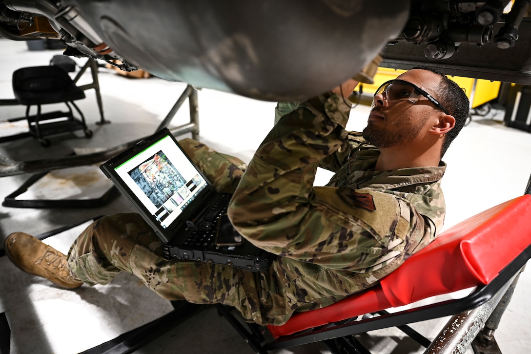 An airman works on the underside of a jet.