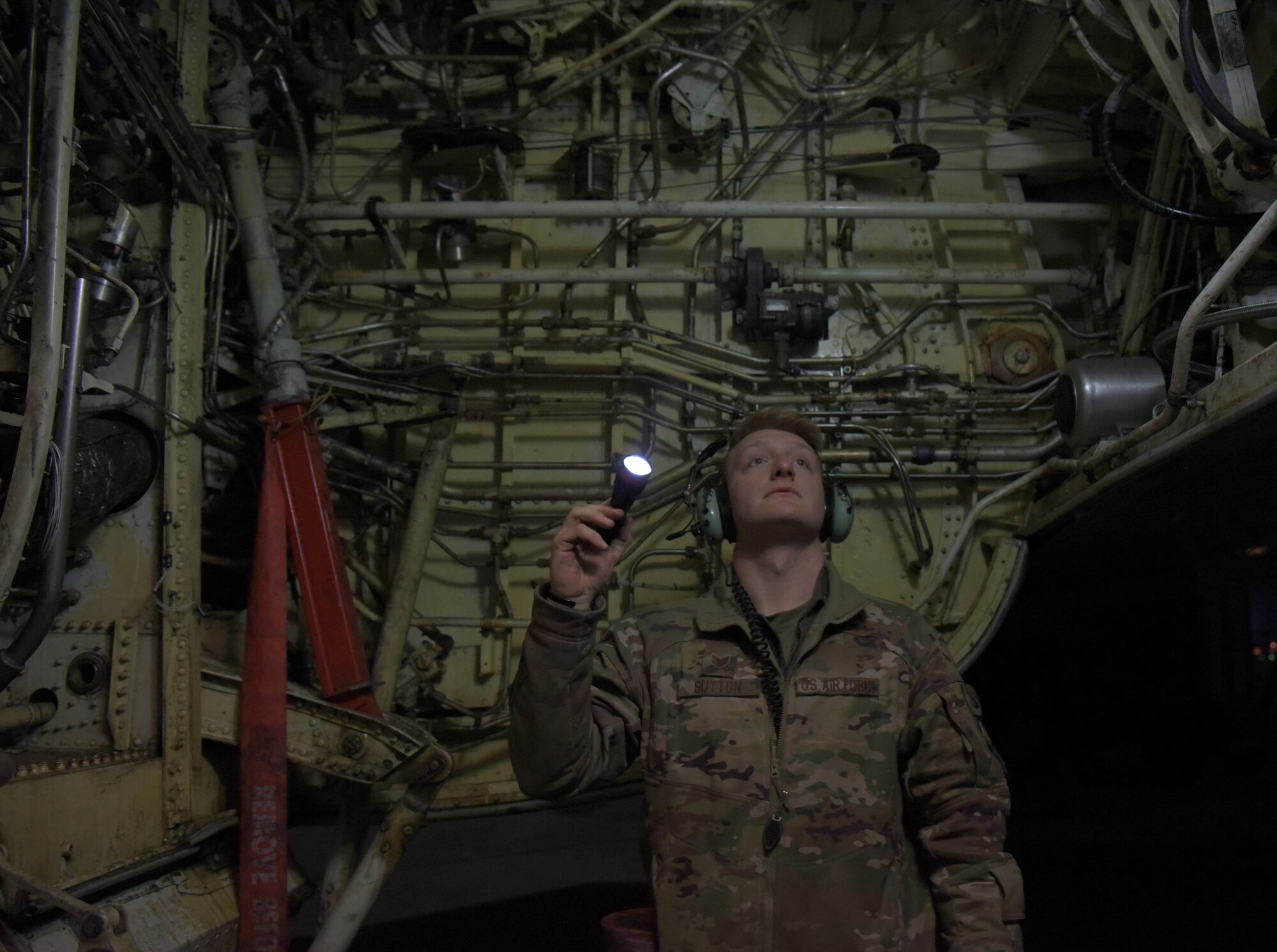 Male U.S. Air Force Airman looks at inside of aircraft with a flashlight