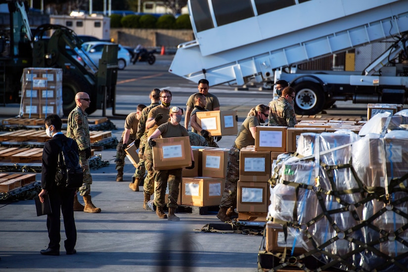 Service members, some wearing face masks, unload boxes.