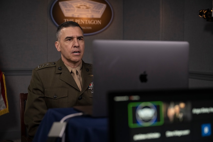 A uniformed servicemember sits behind a laptop computer.