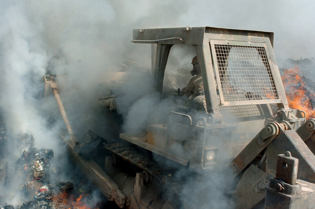 A bulldozer moves through burning rubbish.