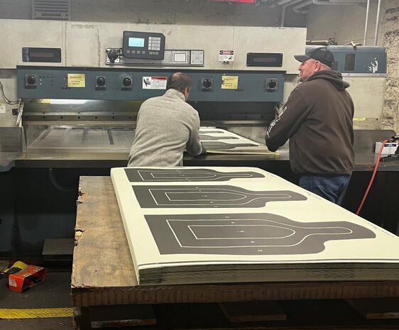 Jerad Vogt and Andrew McWade from Defense Logistics Agency Document Services use a Lawson industrial cutting machine to cut 25-meter silhouette targets while working at a DLA print facility at Rock Island Arsenal, Illinois, March 11, 2022.