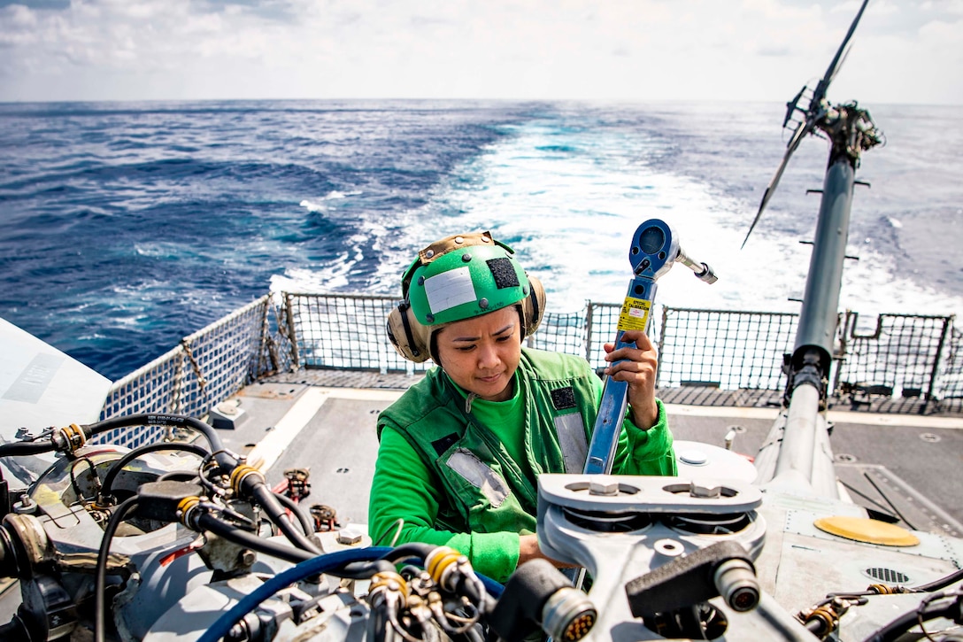 A sailor works on an aircraft on the deck of a ship.