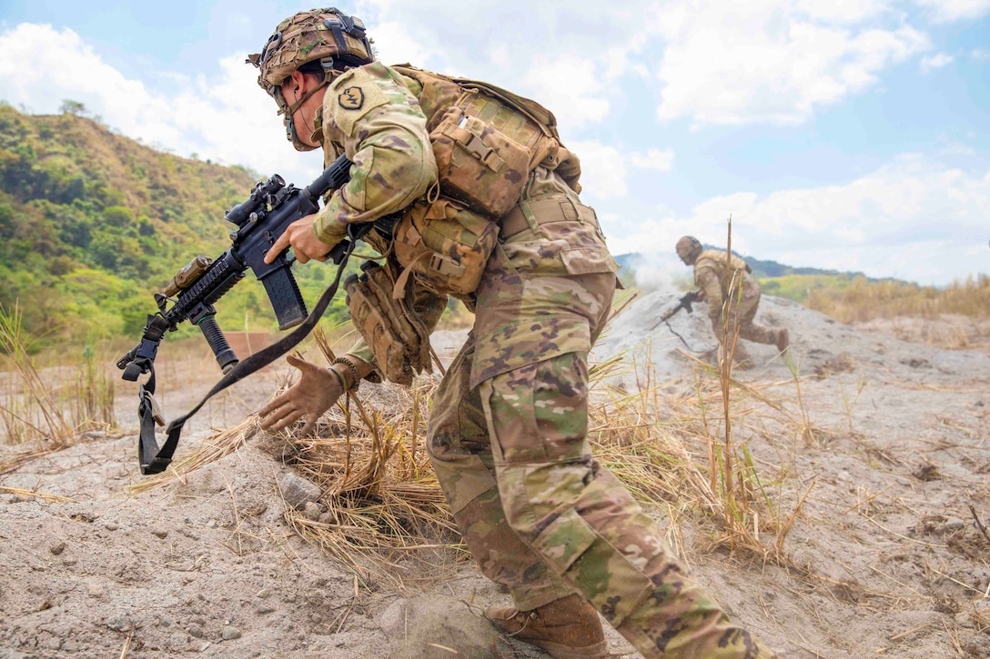 Soldiers move up a dirt hill while holding weapons.