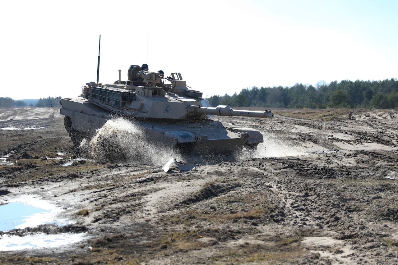 A tank moves across a muddy field.