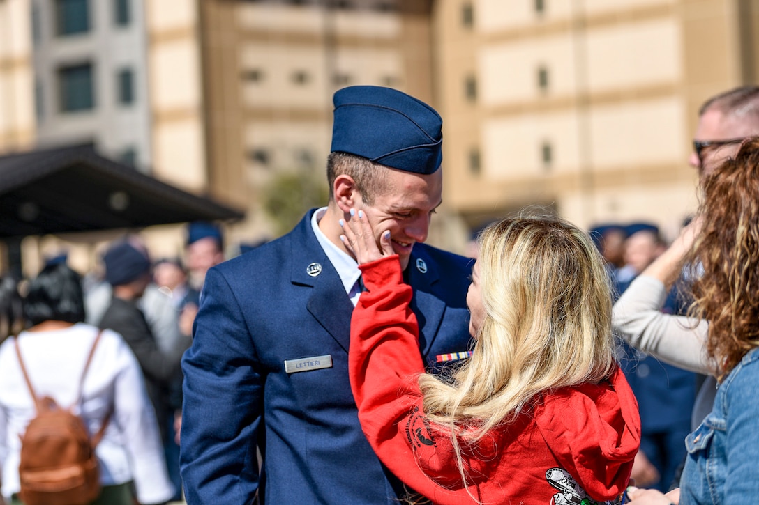 A civilian puts her hand on a service member's face while they embrace in a crowd outside.