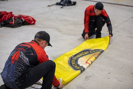 Sgts. 1st Class Michael Johnson (left) and Jeff Menda, with the United States Army Special Operations Command parachute team, the Black Daggers, prepare the 377th Theater Sustainment Command's flag for the next jump at Naval Air Station Joint Reserve Base New Orleans, March 19, 2022.