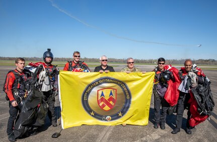 The United States Army Special Operations Command parachute team, the Black Daggers, poses with Maj. Gen. (Ret) Harry "Skip" Philips Jr., 377th Theater Sustainment Commander (2006-2009) and Col. John Stokes Jr., 377th TSC Deployment Support Command Chief of Staff, with the 377th TSC flag during the airshow at Naval Air Station Joint Reserve Base New Orleans, March 19, 2022.