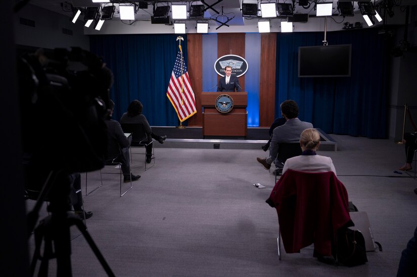 Press secretary stands at lectern and speaks to seated reporters.