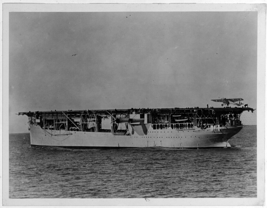 USS Langley (CV-1) at anchor with an Aeromarine 39-B airplane landing on her flight deck, circa 1922. Catalog #: NH 63545.