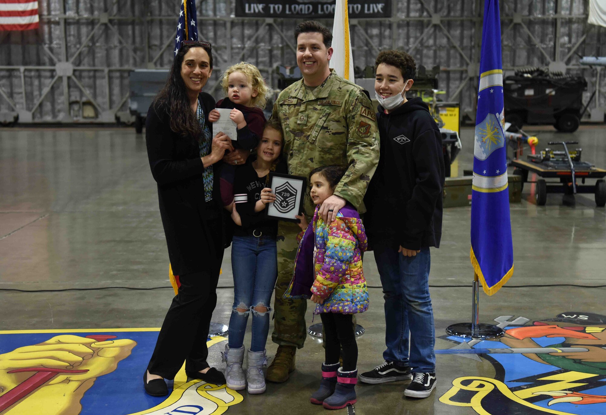 A military member holds up his promotion with friends, family and coworkers