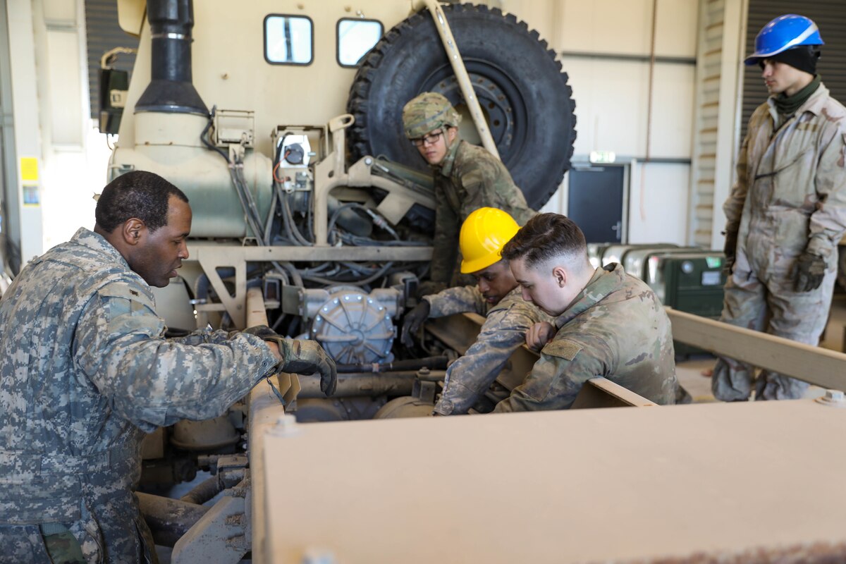 Five service members look at a piece of equipment.