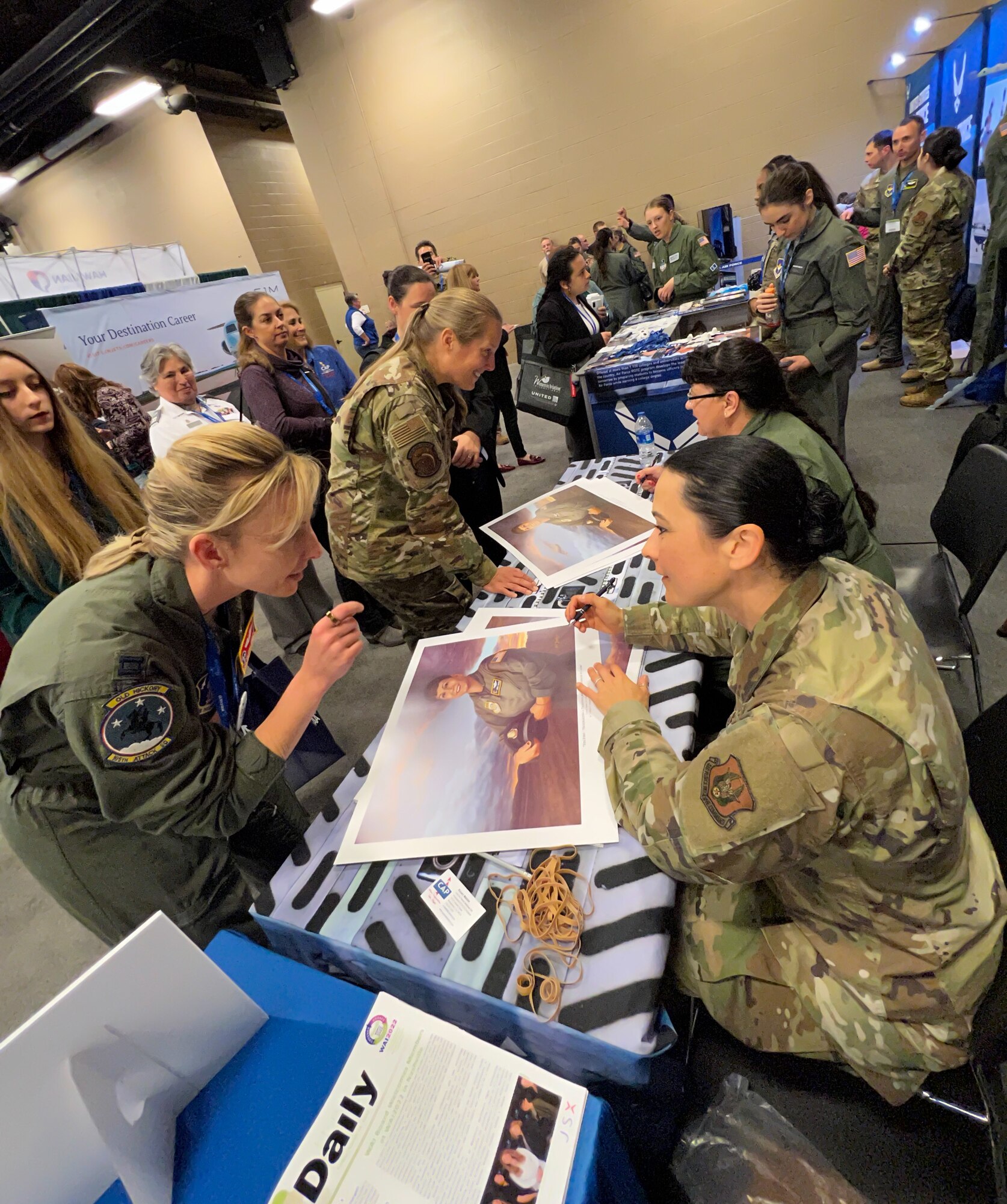 Female Airmen line up to get signatures from U.S. Air Force Reserve Col. (ret.) Kathy Cosand (left), AFRC’s first female pilot, and 2nd Lt. Kat Justen (right), Air Force Reserve Command Office of History and Heritage combat artist