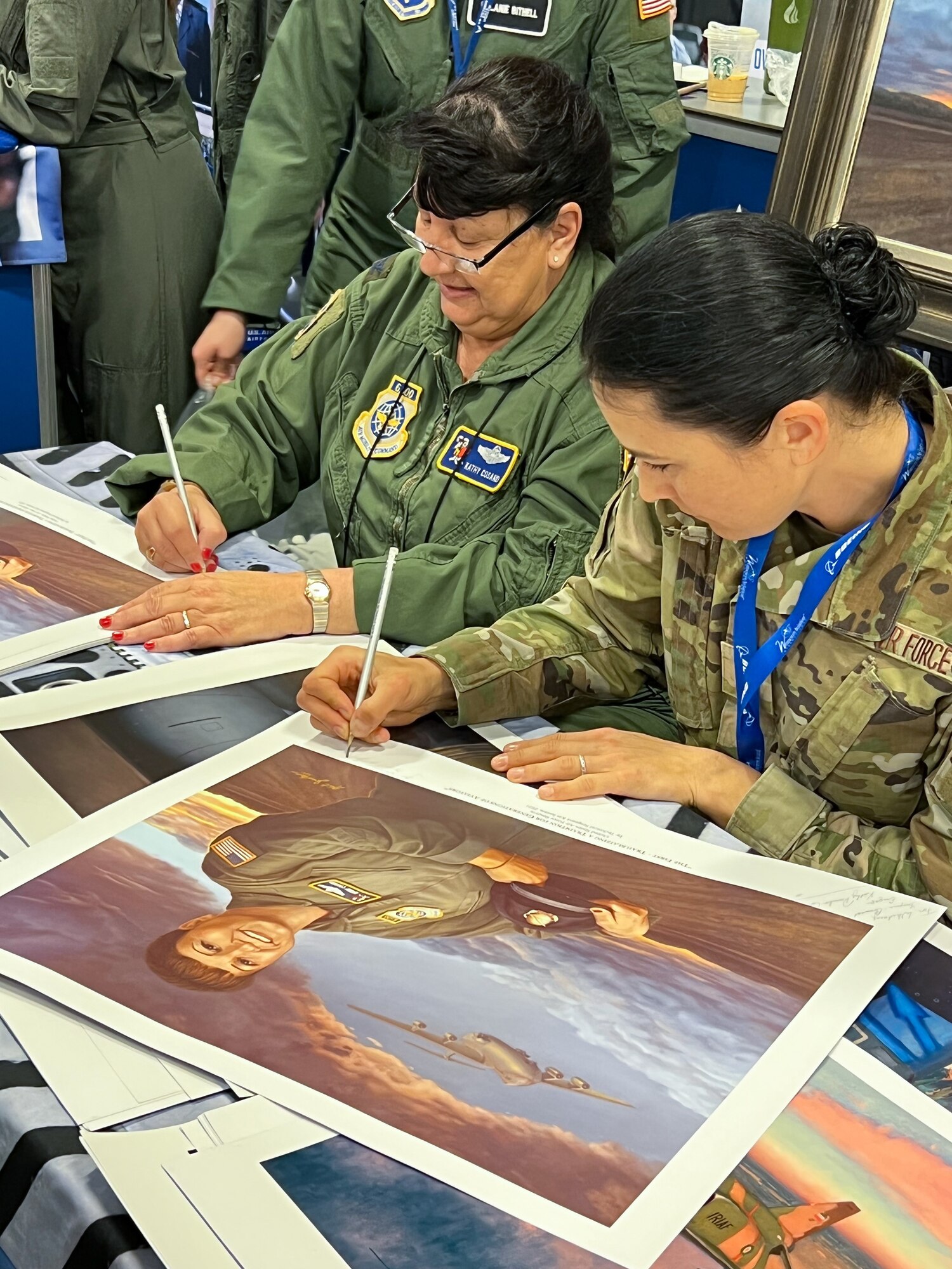 U.S. Air Force Reserve Col. (ret.) Kathy Cosand (left), AFRC’s first female pilot, and 2nd Lt. Kat Justen (right), Air Force Reserve Command Office of History and Heritage combat artist, sign lithographs