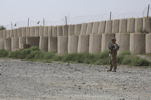 A lone service member stands with a rifle in front of a barricade wall.