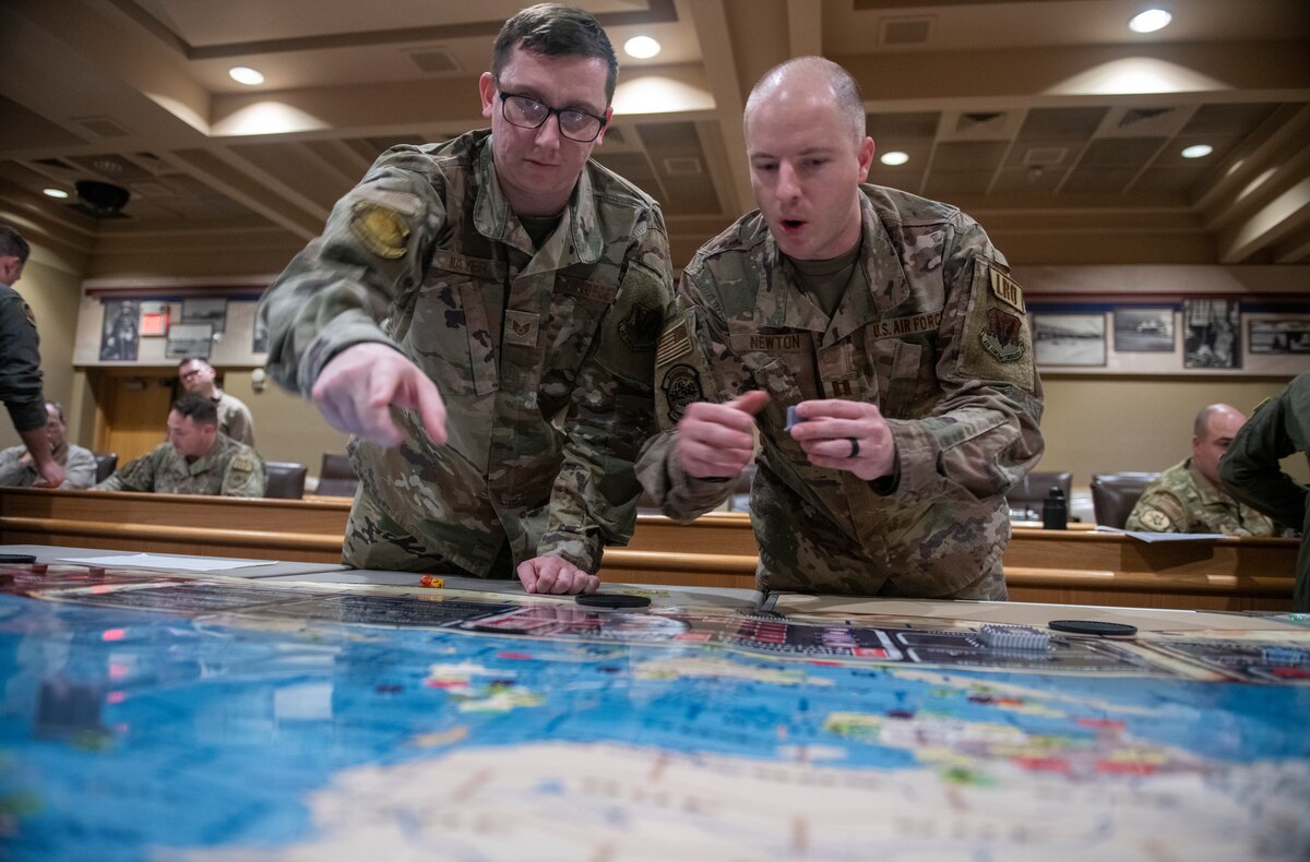 two military members look at a map laid on a table.