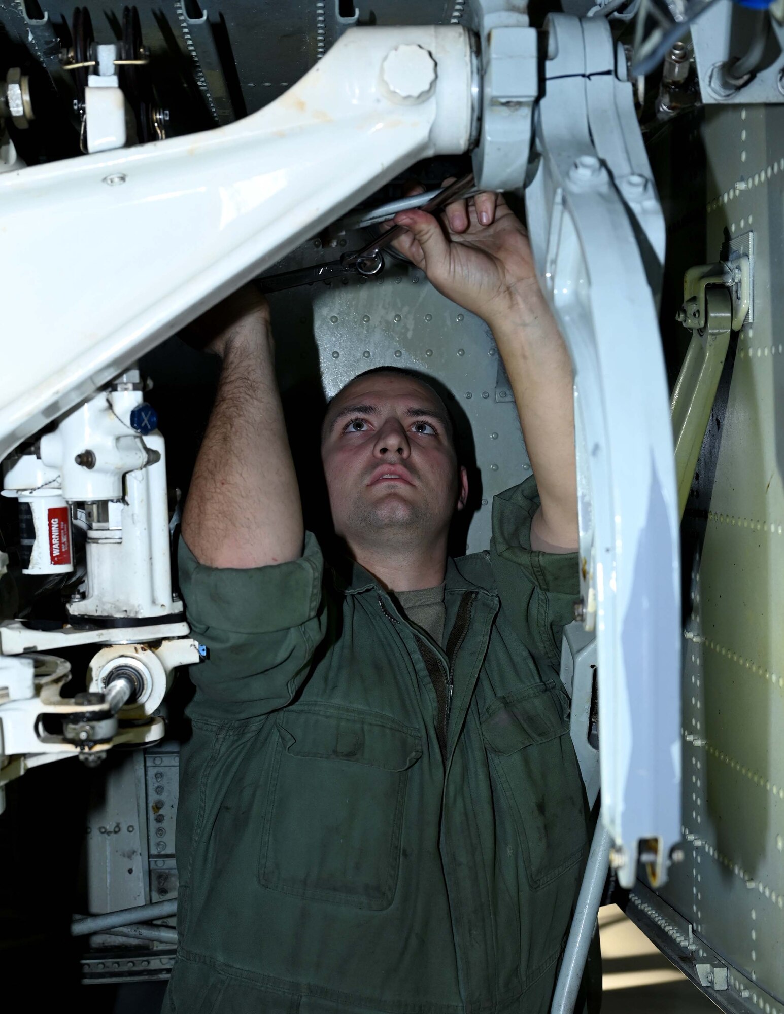 a man uses a ratchet to unscrew a trunnion cap inside the front landing gear of a C-130H Hercules