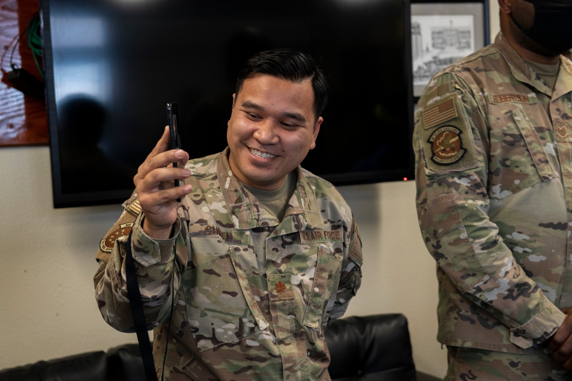 Major Dalin Chhen holds up a phone as his Airman receives his medallion via video call.