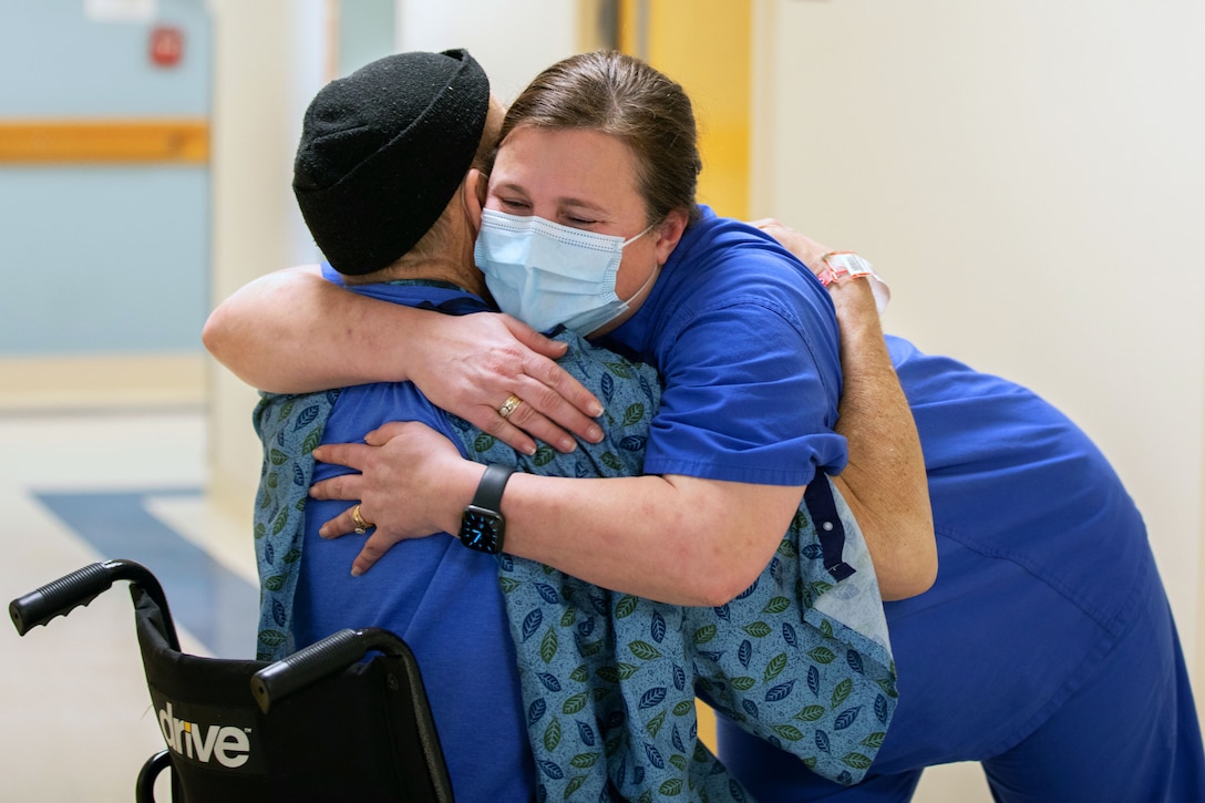 An Air Force nurse wearing a face mask hugs a patient.