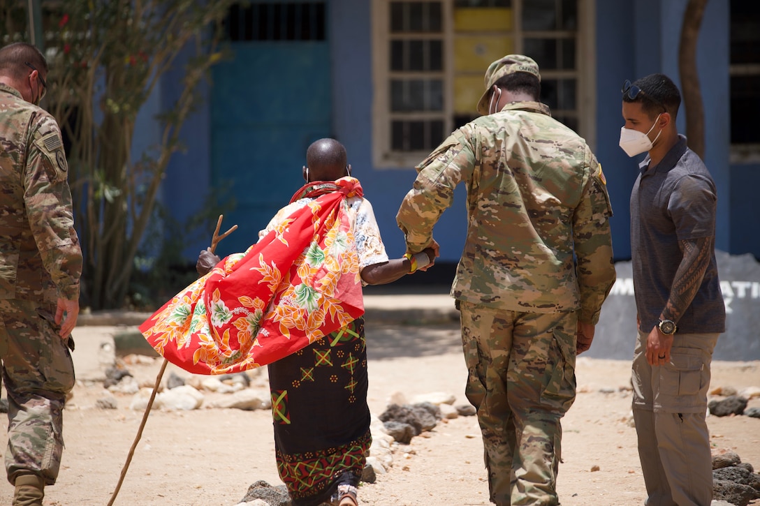 A soldier holds the hand of a Kenyan citizen as they walk away from the camera.