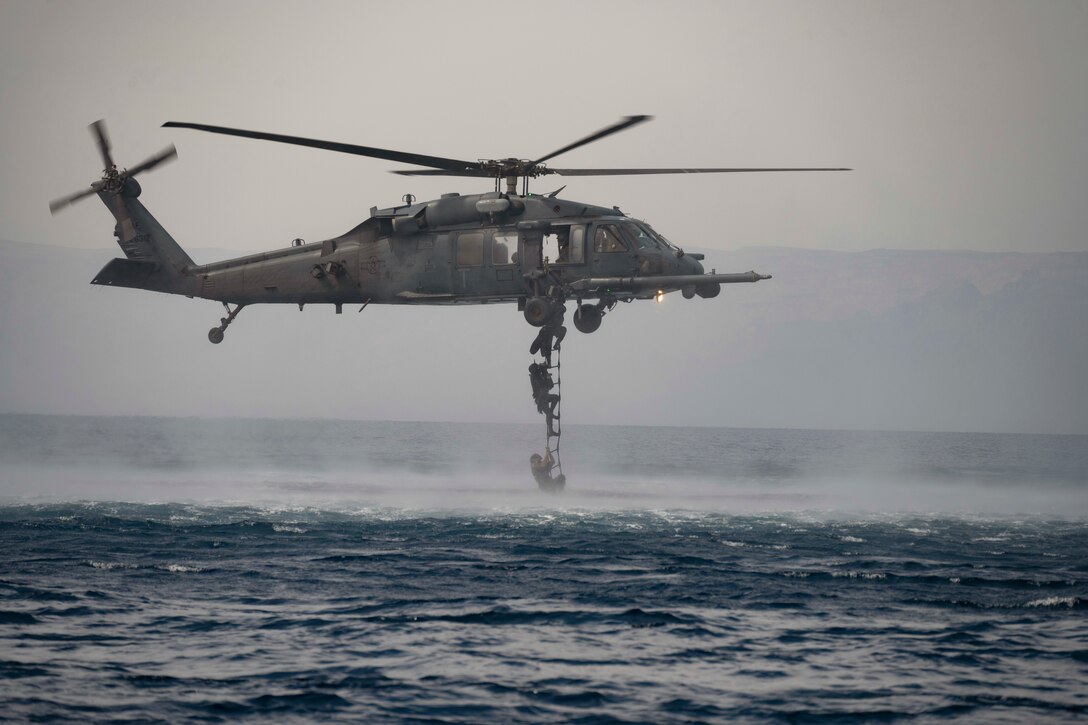 U.S. and Royal Jordanian troops climb out of a body of water onto a ladder attached an airborne helicopter.