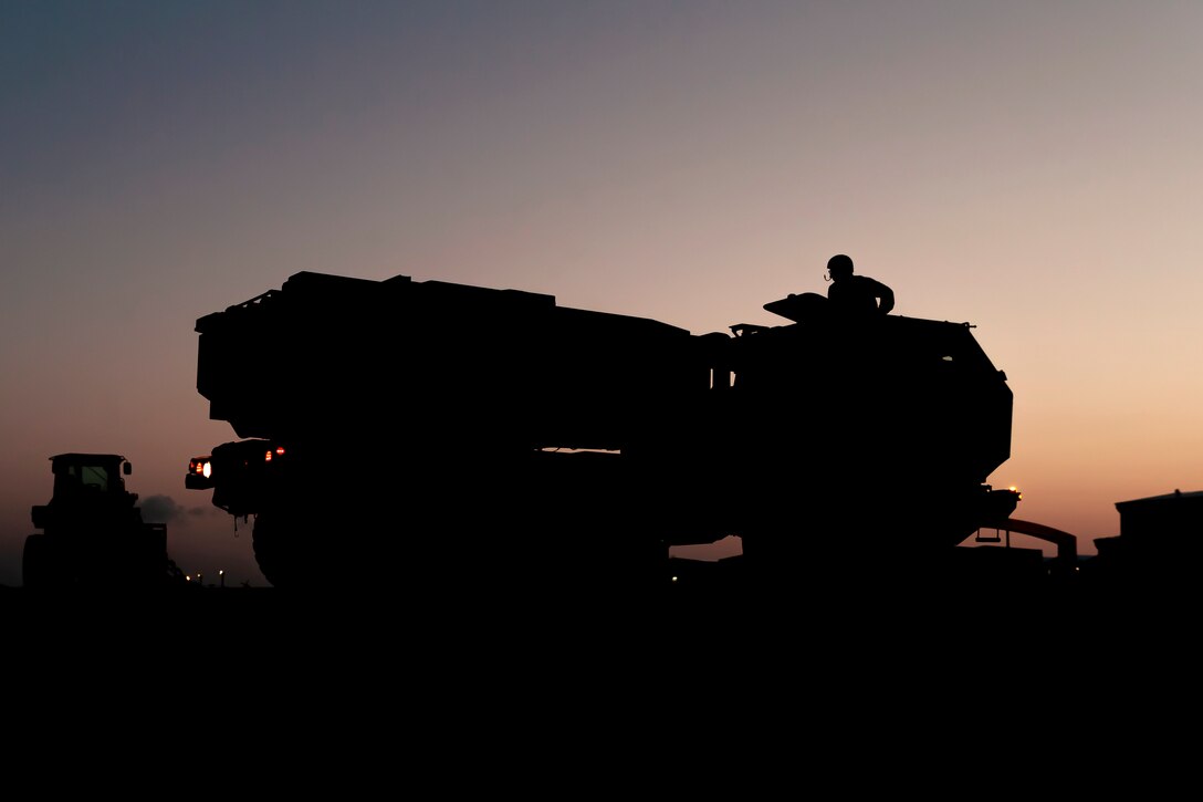 Marines load an armored vehicle onto an aircraft as shown in silhouette.