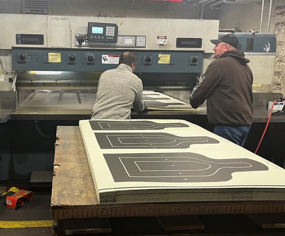 Jerad Vogt and Andrew McWade, Defense Logistics Agency Document Services employees, use a Lawson industrial cutting machine to cut 25-meter silhouette targets while working at a DLA printing facility at Rock Island Arsenal, Ill., March 11, 2022. The Defense Logistics Agency is now the Defense Department’s primary provider of printing services, office print devices and electronic conversion services. (Defense Logistics Agency photo by John Turner)