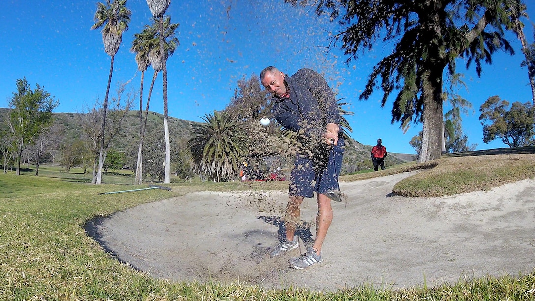 Wounded warrior hits golf ball out of sand trap.