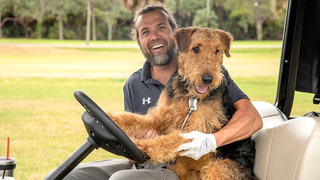 Wounded warrior rides a golf car with his service dog.