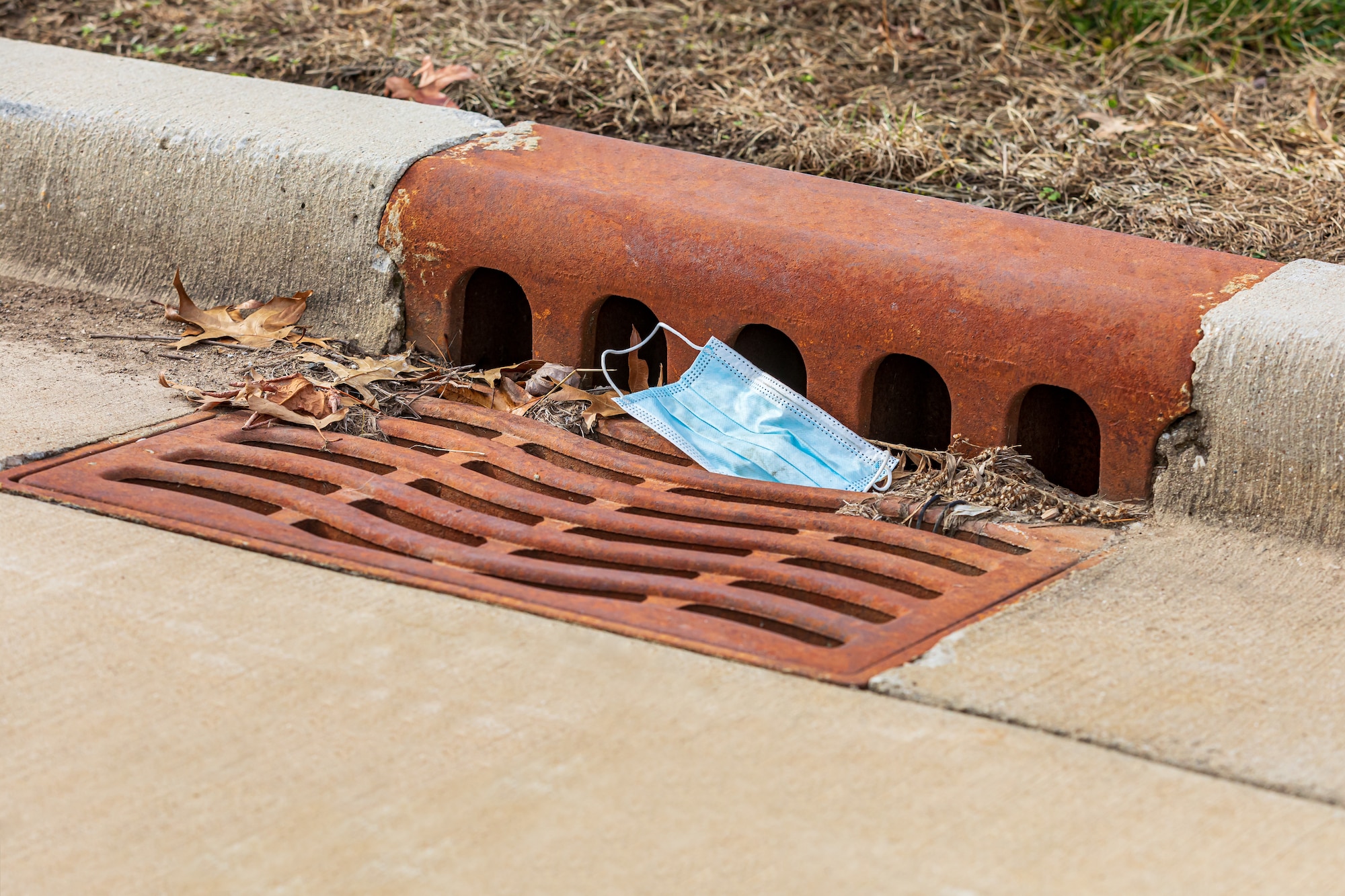Photo shows a stormwater drain with a mask caught in the grate.