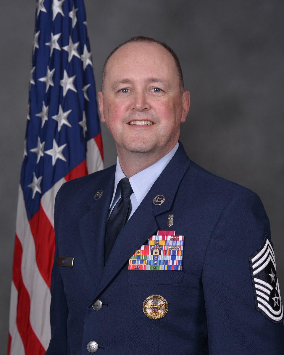 Head shot of male Airman in front of an American flag.