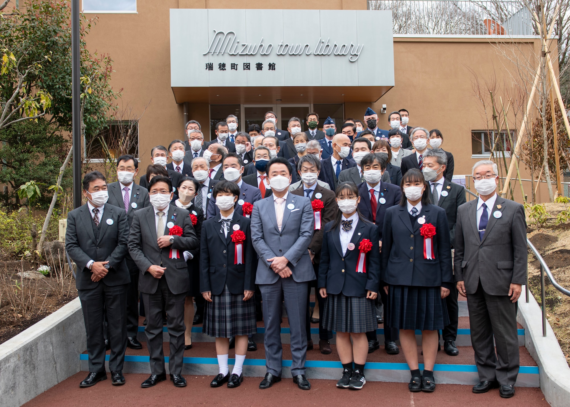 A large group of Japanese city officials and local students pose in front of a library