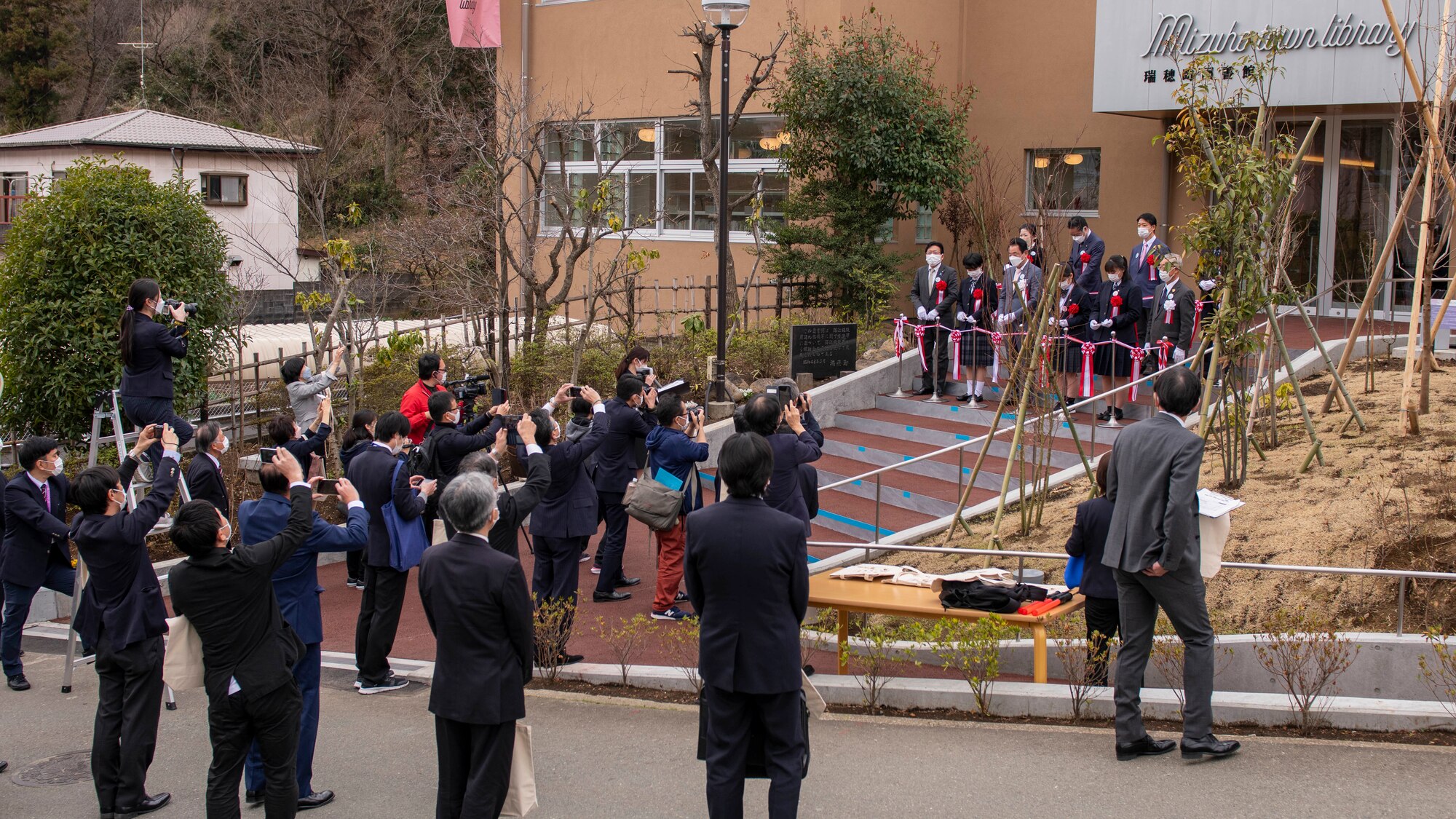 A crowd of onlookers wait for a ribbon cutting ceremony at a local library.