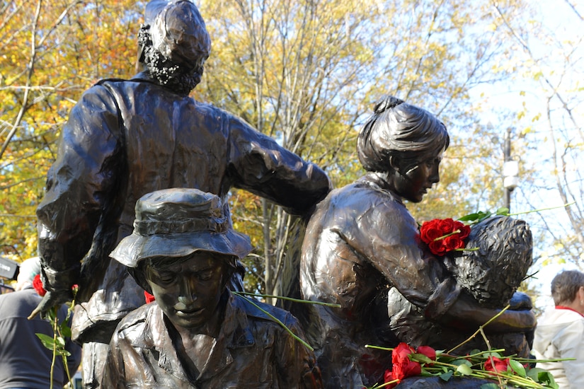 A nurse cradling an injured soldier, a woman looking skyward, and (foreground) a kneeling woman holding a helmet.