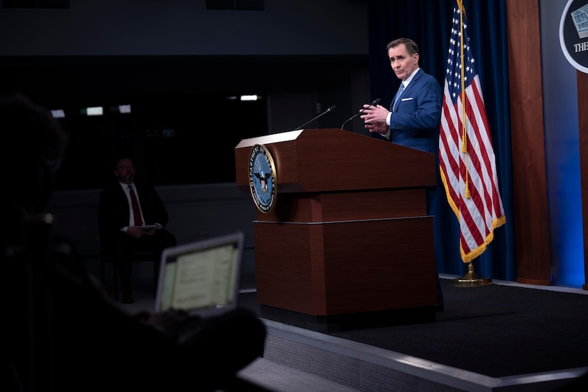 A man speaks from behind a large podium with an American flag behind him.