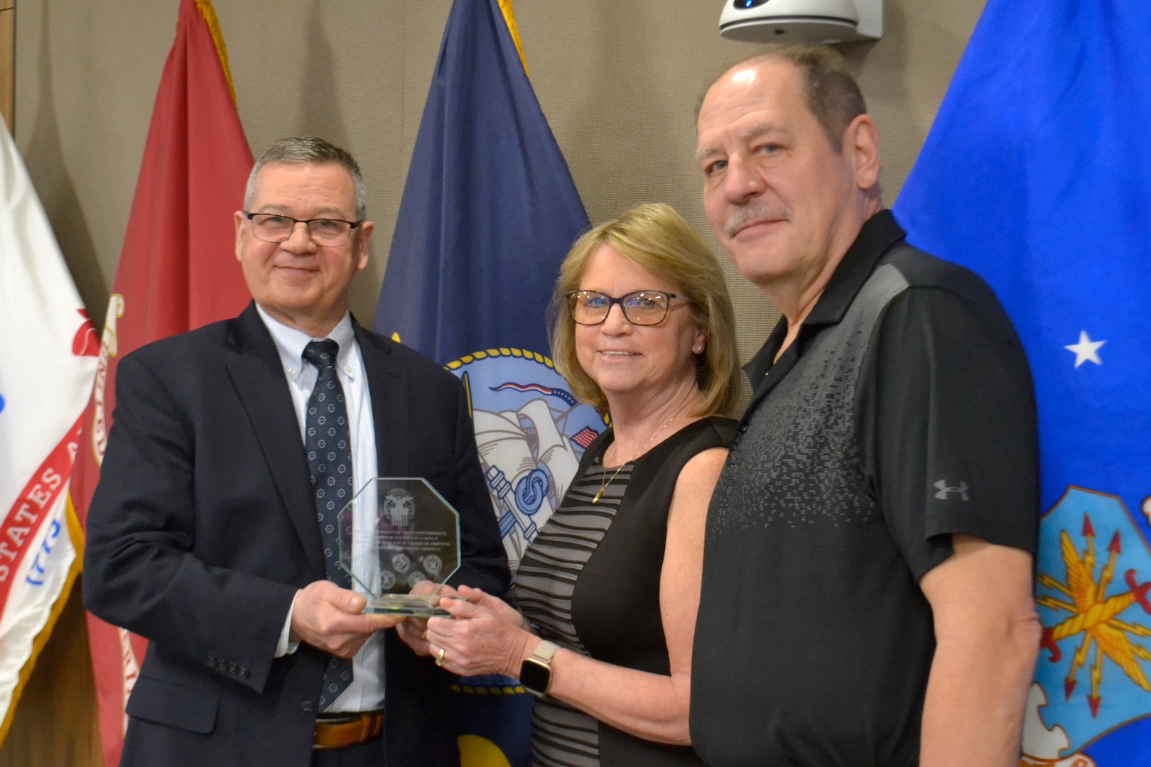 Defense Logistics Agency Troop Support Deputy Commander Richard Ellis, left, presents Shirley Kyser, center, with a retirement memento, with her husband Michael Szatkowski during a retirement ceremony March 21, 2022, in Philadelphia. Kyser is retiring after 31 years of service with the organization.