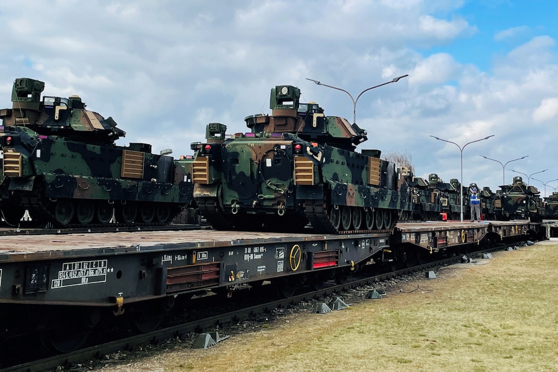 A line of tanks sit atop rail cars.
