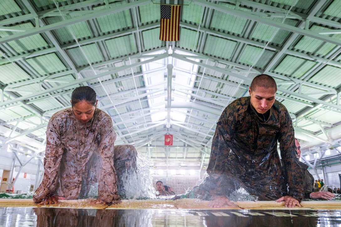 Two Marines kneel next to each other in wet uniforms.