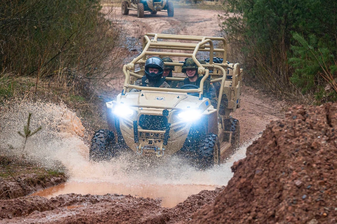 Airmen drive military vehicle through muddy water.