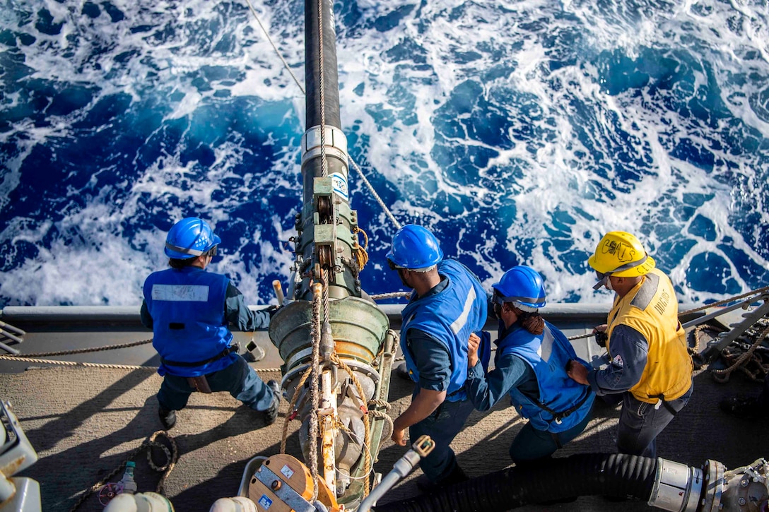 Sailors rig a line on the deck of a ship.