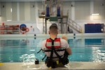 A prospective Coast Guard rescue swimmer sits at the edge of a training pool with their back to the camera