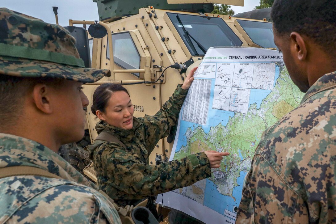 A Marine talks and points at a map she's holding against a vehicle as two fellow Marines listen.