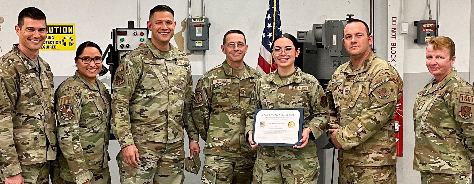 A female in uniform is receiving an award from of group of uniformed personnel.